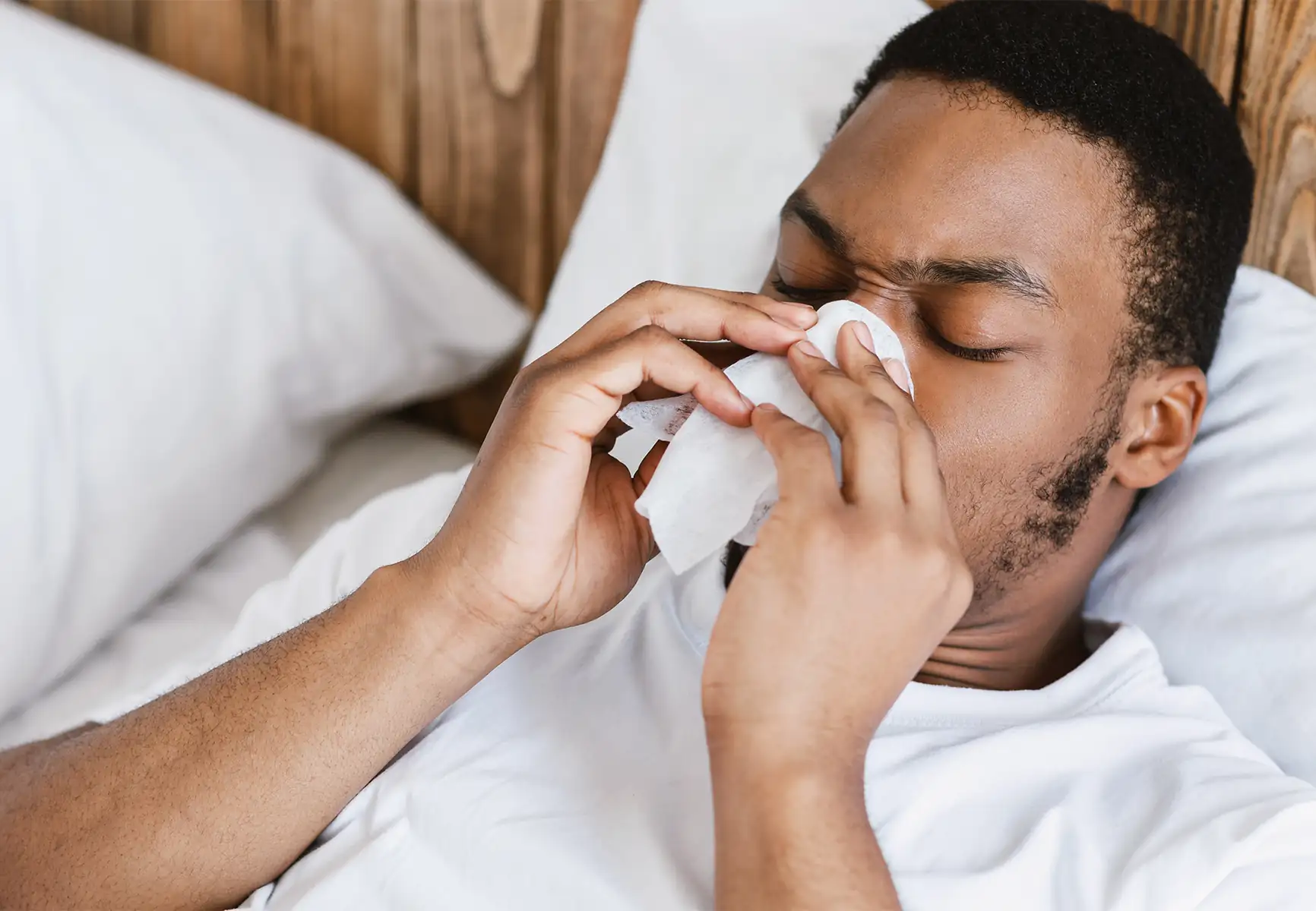 Man blowing nose in bed