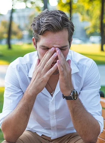 Man holding sinuses while sitting on park bench