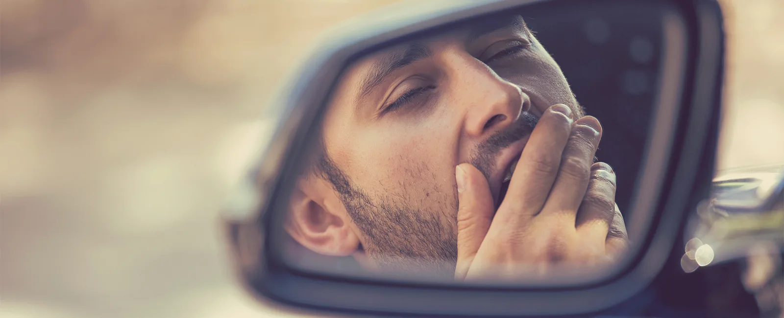Man yawning in car mirror