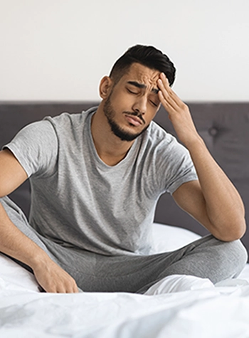 Young man holding hand to his head while sitting in bed