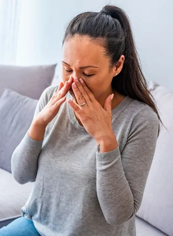 40s woman sitting on couch holding her nose