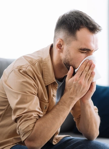 Man blowing his nose while sitting on the couch