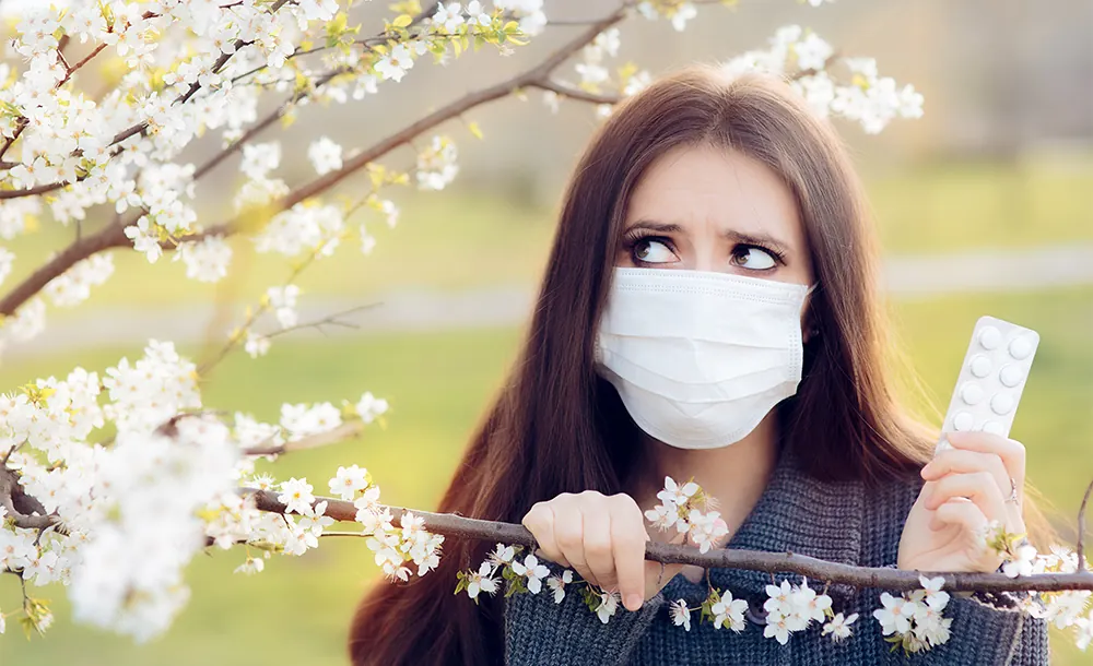 woman outdoors next to tree holding allergy pills