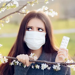 woman outdoors next to tree holding allergy pills